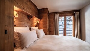A wooden cabin-style bedroom with a large bed, two wall-mounted lamps, and a window with curtains.