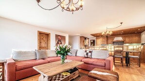 A modern living room with a wooden coffee table, a red sofa, and a kitchen area with wooden cabinets and a dining set.