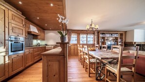 A wooden kitchen with a central island, wooden cabinets, and a dining area with chairs and a table.