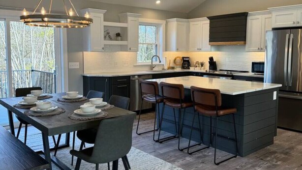 Una cocina moderna con una isla central, taburetes de bar y una mesa de comedor para seis personas.