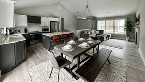 Una cocina moderna con comedor, que cuenta con una isla grande, piso de madera oscura y una araña.