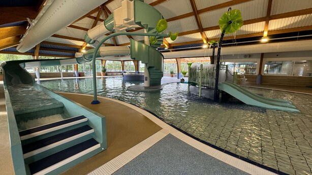 Ein großer Indoor-Wasserpark mit Rutschen, einem Schwimmbecken und einem überdachten Bereich mit Sitzgelegenheiten.