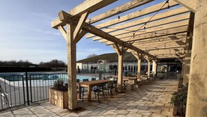 Eine Terrasse im Freien mit hölzernen Pergolen, Steinböden und Sitzbereichen mit Blick auf einen Swimmingpool.