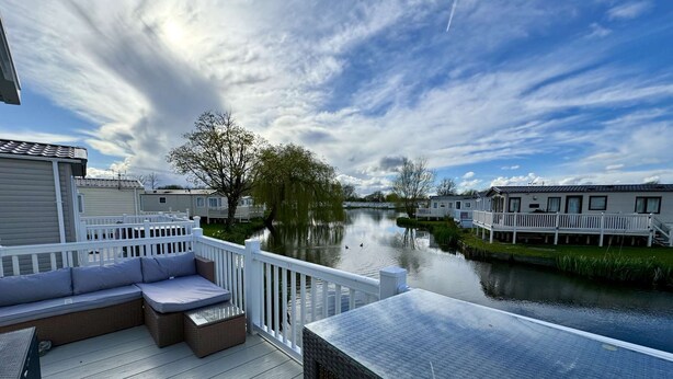 Una terraza con un sofá y una mesa, con vista a un río tranquilo y casas al fondo.