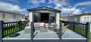 Ein überdachter Außenbereich mit Korbmöbeln, ein kleines Gebäude mit Antenne und eine umzäunte Terrasse.