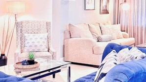 A living room with a blue sofa, a patterned armchair, a glass coffee table, and a chandelier. - The Miami Grove Oasis (Miami)
