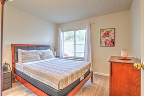 Quarto com estrutura de cama de madeira, mesa de cabeceira, janela com cortinas e um pequeno armário.