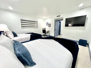 Una habitación de hotel con dos camas, un escritorio, una silla, un televisor y una puerta.