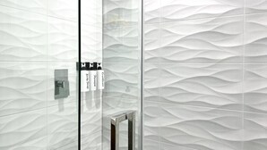 Une salle de bain avec un mur au revêtement texturé, une douche en verre et un porte-serviettes avec des bouteilles.