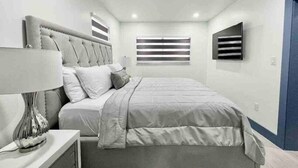 Une chambre moderne avec un grand lit, une table de chevet avec une lampe et une fenêtre avec des stores.