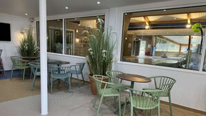An indoor seating area with green chairs and tables, large windows, and indoor plants.