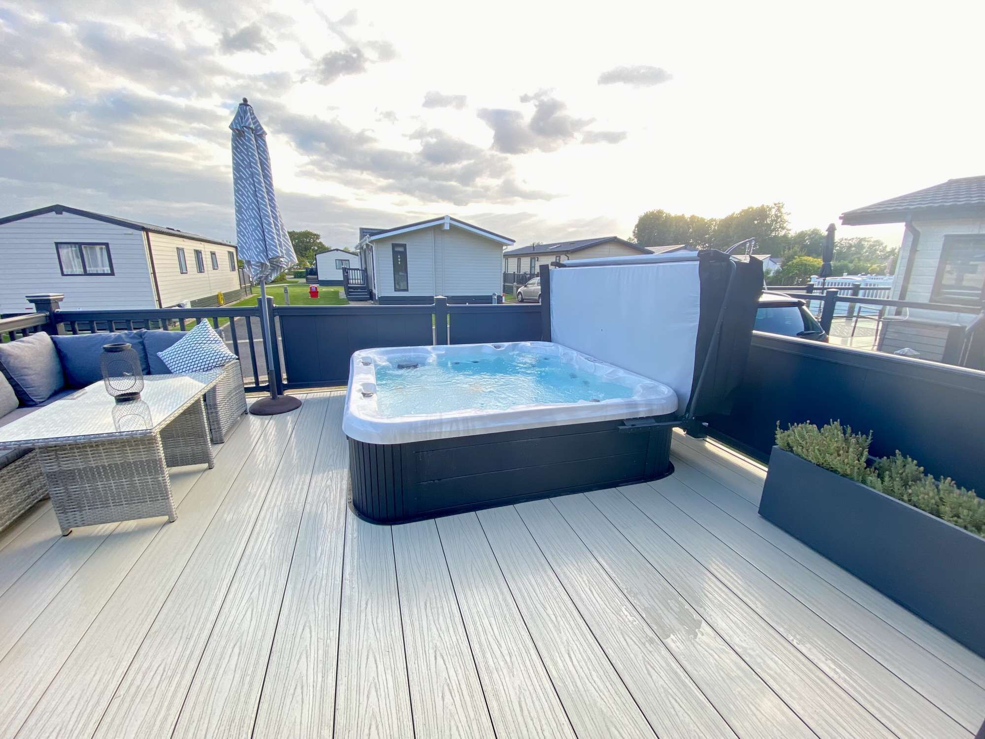A hot tub on a wooden deck with outdoor furniture and a covered area.