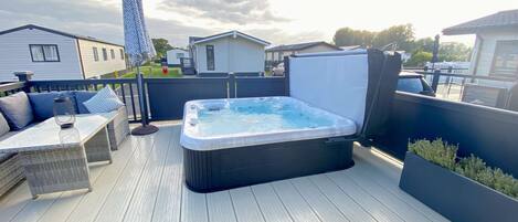 A hot tub on a wooden deck with outdoor furniture and a covered area.