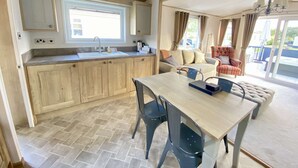A compact kitchen with wooden cabinets, a sink, and a dining area with a table and chairs. - Burford Hot Tub Holiday Home (Hoburne Holiday Park)