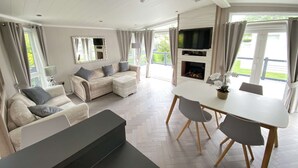 A spacious living room with a sofa, a dining table, and a fireplace. - Spring Lodge with private hot tub (Hoburne Holiday Park)