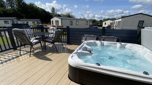 Een terras met een jacuzzi, tuinmeubilair en zicht op stacaravans in de verte.