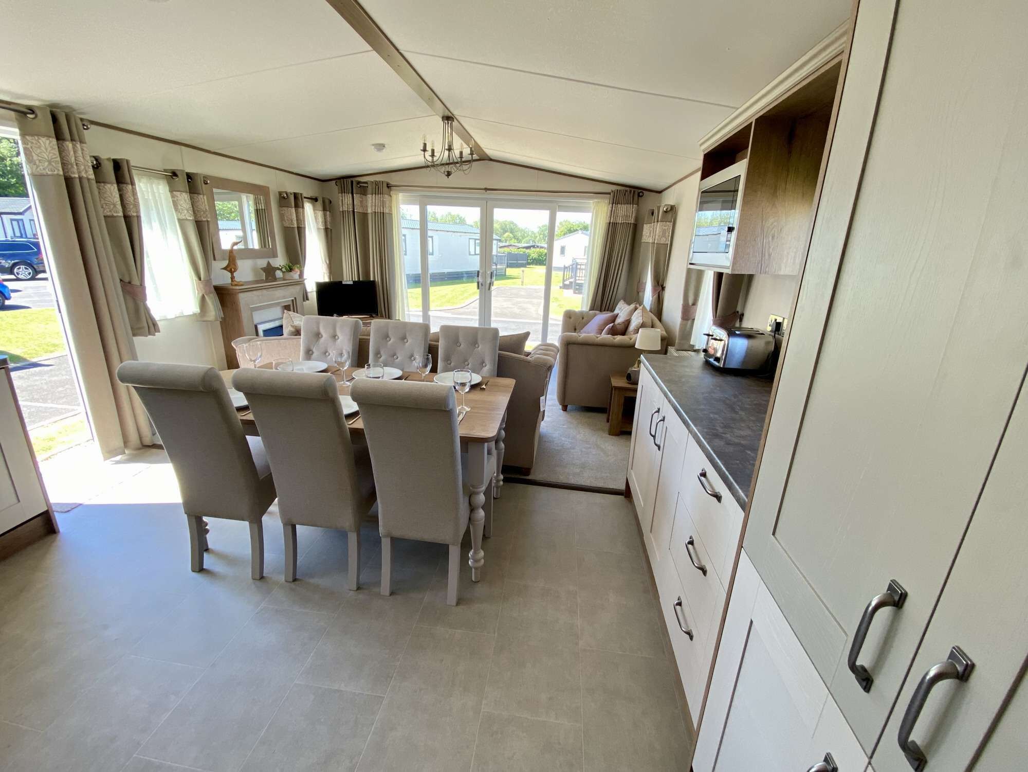 A spacious living area with a dining table, comfortable seating, a kitchen area, and large windows offering a view of the outdoors.