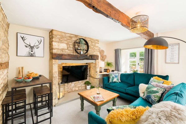 A cozy living room with a stone fireplace, teal sofa, wooden coffee table, and a dining area with a rustic table and chairs. - Why Not, in the heart of the Cotswolds (Stow on the Wold)