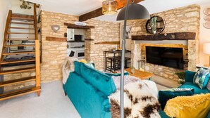 Una sala de estar acogedora con una pared de piedra, una chimenea, un sofá color turquesa y una escalera de madera.