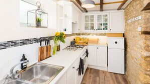 Cocina moderna con armarios blancos, estufa a gas y pared de piedra.