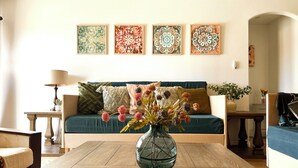 A living room with a wooden coffee table, a sofa with cushions, a vase with flowers, and three framed artworks on the wall. - House on the Mesa with 9 beds/Jacuzzi & Pool near JTNP (Yucca Valley)