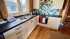 A kitchen with wooden cabinets, a stainless steel sink, and a tiled backsplash. - Lilly Lodge on the edge of Lake Pochard (Lake Pochard)