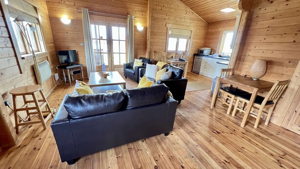 A cozy cabin interior with a sofa, dining table, and kitchen area. - Lilly Lodge on the edge of Lake Pochard (Lake Pochard)