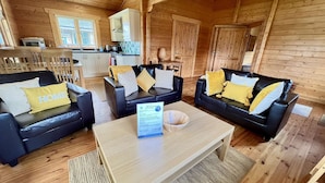 A cozy cabin interior with two black leather sofas, each with a 'HOME' pillow, a wooden coffee table, and a welcome sign. - Lilly Lodge on the edge of Lake Pochard (Lake Pochard)