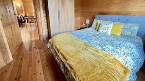 A wooden cabin bedroom with a bed, a wardrobe, and a small table with chairs. - Lilly Lodge on the edge of Lake Pochard (Lake Pochard)