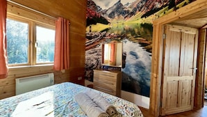 A room with a bed, a dresser, a window with curtains, and a mural of a mountain landscape.
