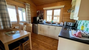 A wooden cabin kitchen with a dining table, chairs, a microwave, a sink, and cabinets.