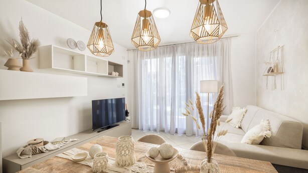 A modern living room with a wooden dining table, white sofas, and pendant lights. - Neu Eingerichtetes Apartment mit Pool, Fitnessstudio und Sauna, Nähe Bardolino (Cavaion Veronese)