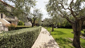A paved pathway flanked by neatly trimmed hedges and trees, leading to a residential area with houses and a well-maintained lawn. - Neu Eingerichtetes Apartment mit Pool, Fitnessstudio und Sauna, Nähe Bardolino (Cavaion Veronese)