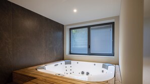 A modern bathroom with a wooden floor, a large bathtub, and a window with blinds. - Neu Eingerichtetes Apartment mit Pool, Fitnessstudio und Sauna, Nähe Bardolino (Cavaion Veronese)