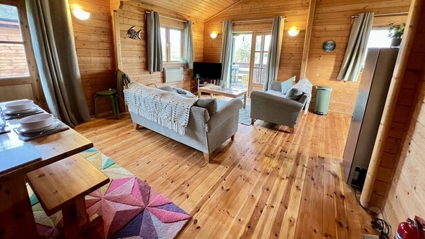 Una cabaña acogedora con interior de madera, un sofá, una mesa de comedor y un televisor.