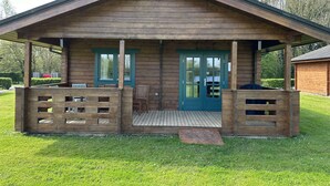 Una cabaña de madera con un porche, dos puertas y una pequeña terraza.