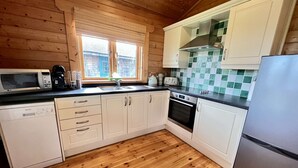 Una cocina moderna con suelo de madera, armarios blancos, un refrigerador de acero inoxidable y una ventana con persianas.