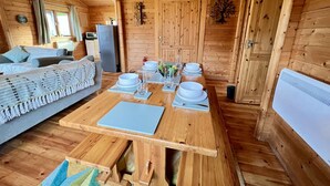 Interior acogedor de una cabaña de madera con una mesa de comedor para cuatro personas, un sofá y una zona de cocina.