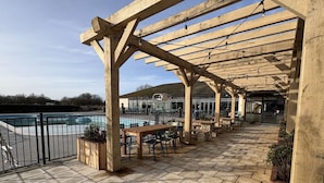 An outdoor patio with wooden pergolas, stone flooring, and seating areas overlooking a swimming pool. - Bumble Bee Cabin on Heron Lake (Hoburne Holiday Park)
