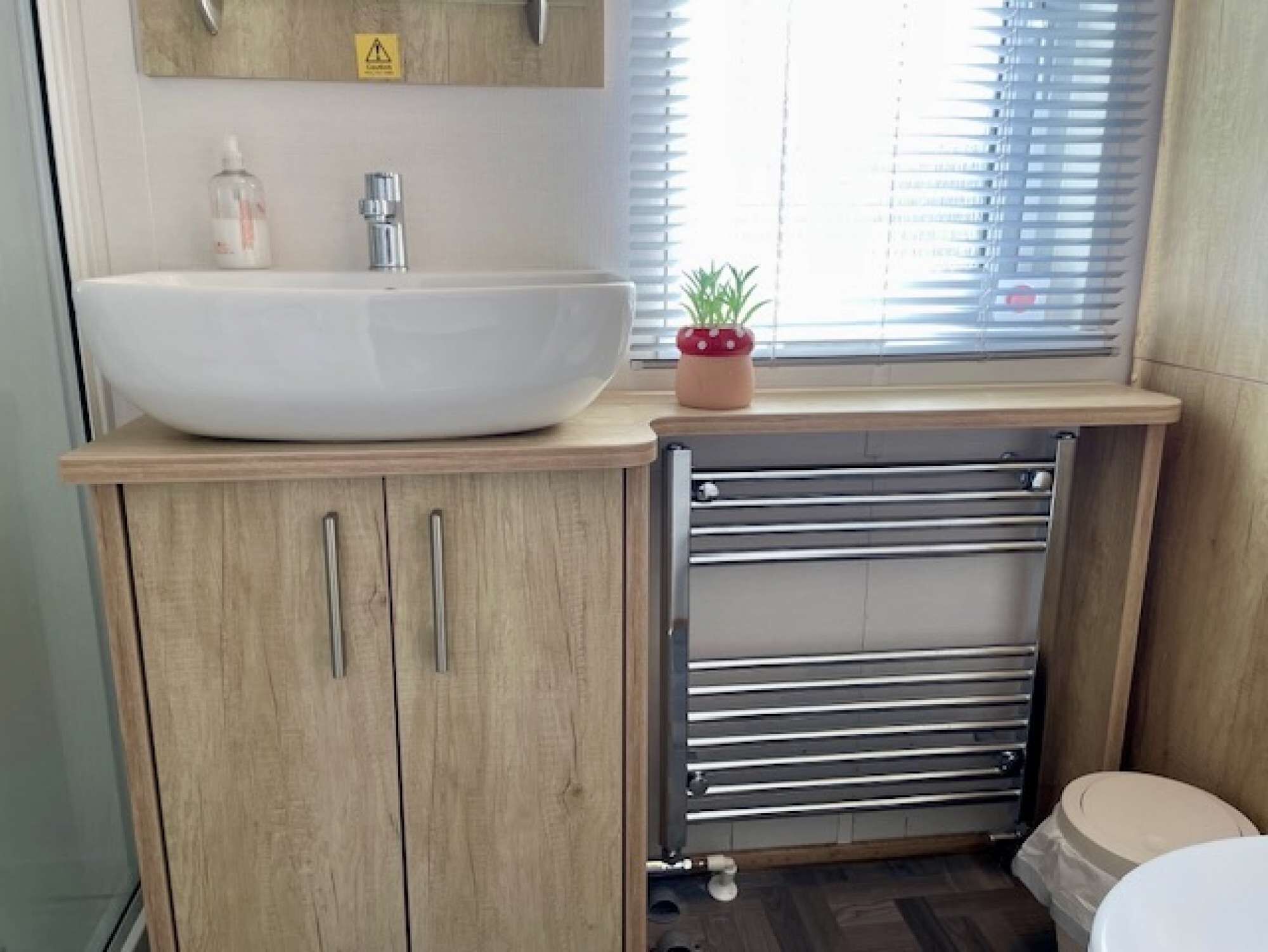 Un baño con lavamanos blanco, armarios de madera, toallero y retrete.