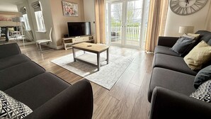 Una sala de estar moderna con un sofá, una mesa de centro, un televisor y un balcón con cortinas.