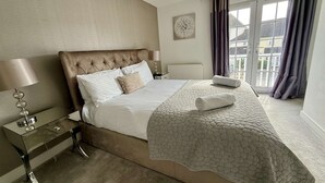 Un dormitorio con una cama grande, una mesita de noche con lámpara, un radiador y una ventana con cortinas.