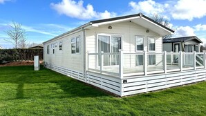 Une maison mobile dotée d’une terrasse, de grandes fenêtres et d’une cour clôturée.