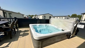 A hot tub on a wooden deck with a table and chairs, surrounded by a black fence.