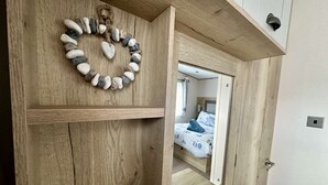 A wooden wardrobe with a mirror reflecting a bed with a patterned bedspread.