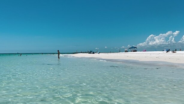A beach with clear turquoise water, white sand, and a few people in the distance.