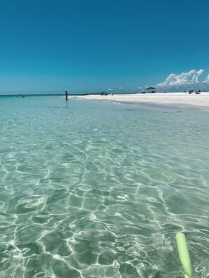 A beach with clear turquoise water, white sand, and a few people in the distance. - Island 🏝️ Escape on Private Street – 5 min Walk to Beach & Dining (Holmes Beach)