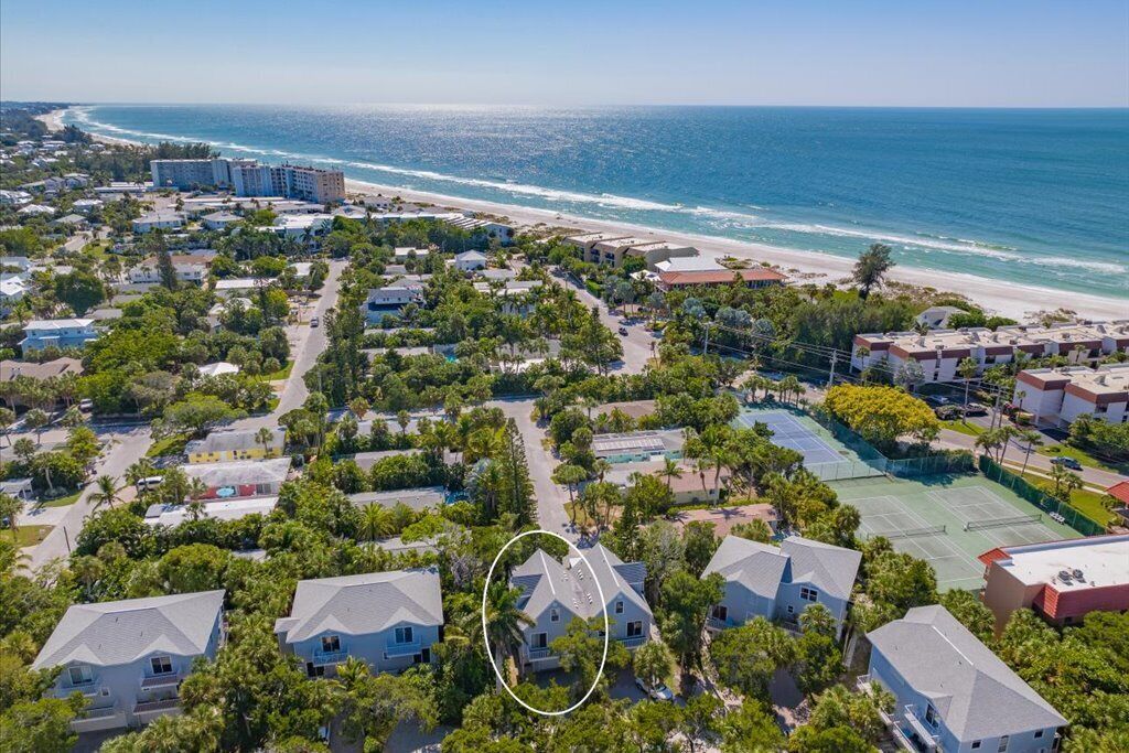 Luftaufnahme einer Küstenwohngegend mit Häusern, einem Strand und einem Tennisplatz.