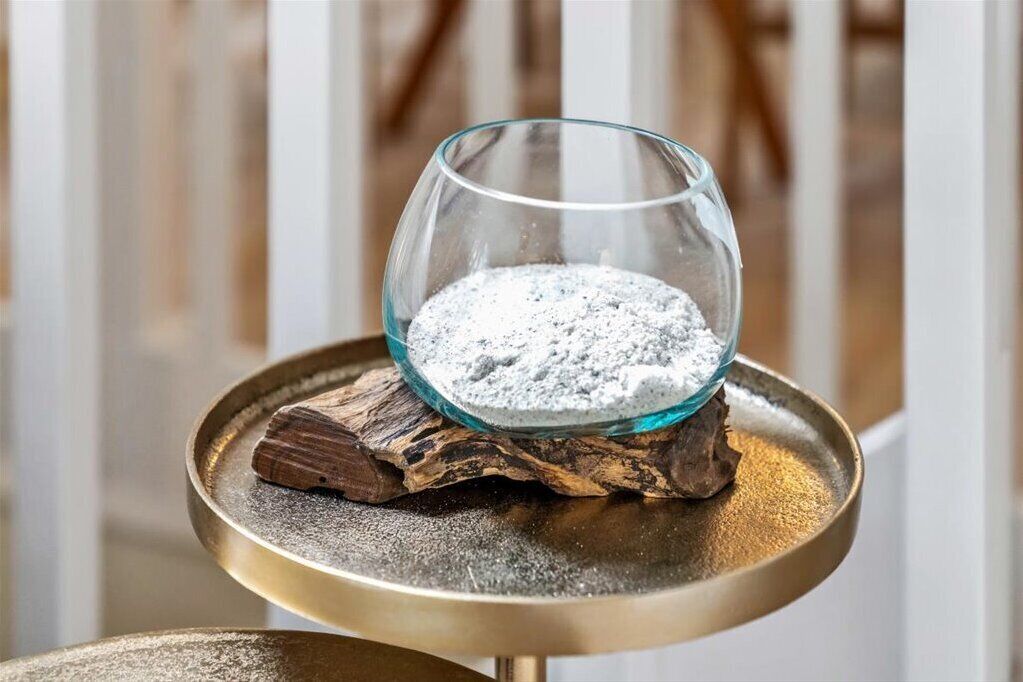 A glass bowl filled with white powder on a wooden coaster, placed on a metallic tray.
