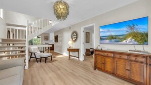 A spacious living area with a wooden floor, a staircase, a large flat-screen TV, and a dining area with a table and chairs.